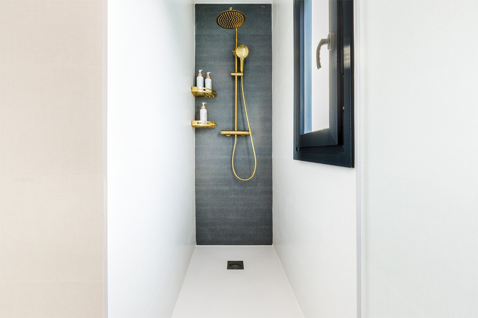 Ducha con plato blanco, columna dorada y pared de gres gris