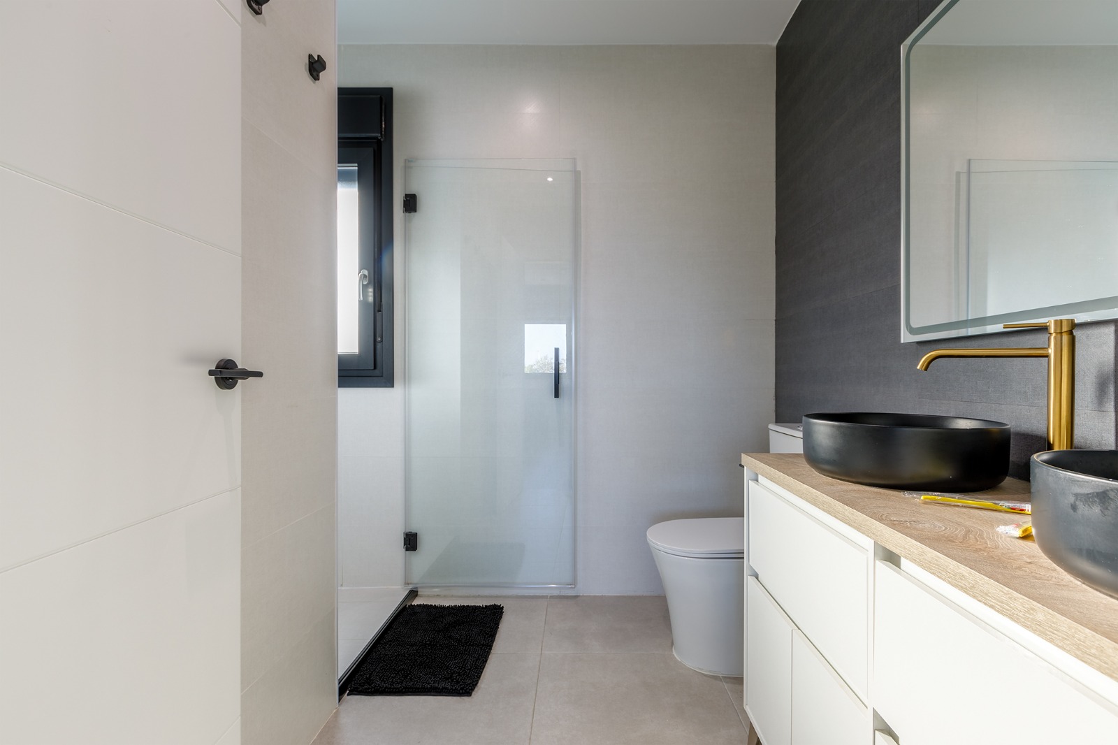 Baño en suite con ducha, doble lavabo de cerámica negra y grifería dorada