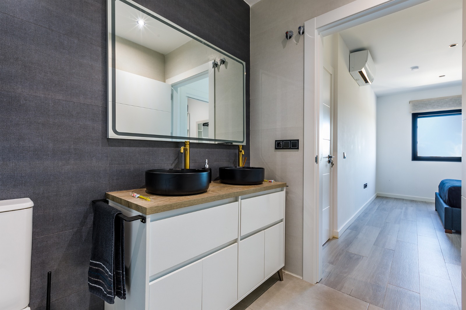 Baño en suite con doble lavabo negro, espejo y salida al dormitorio