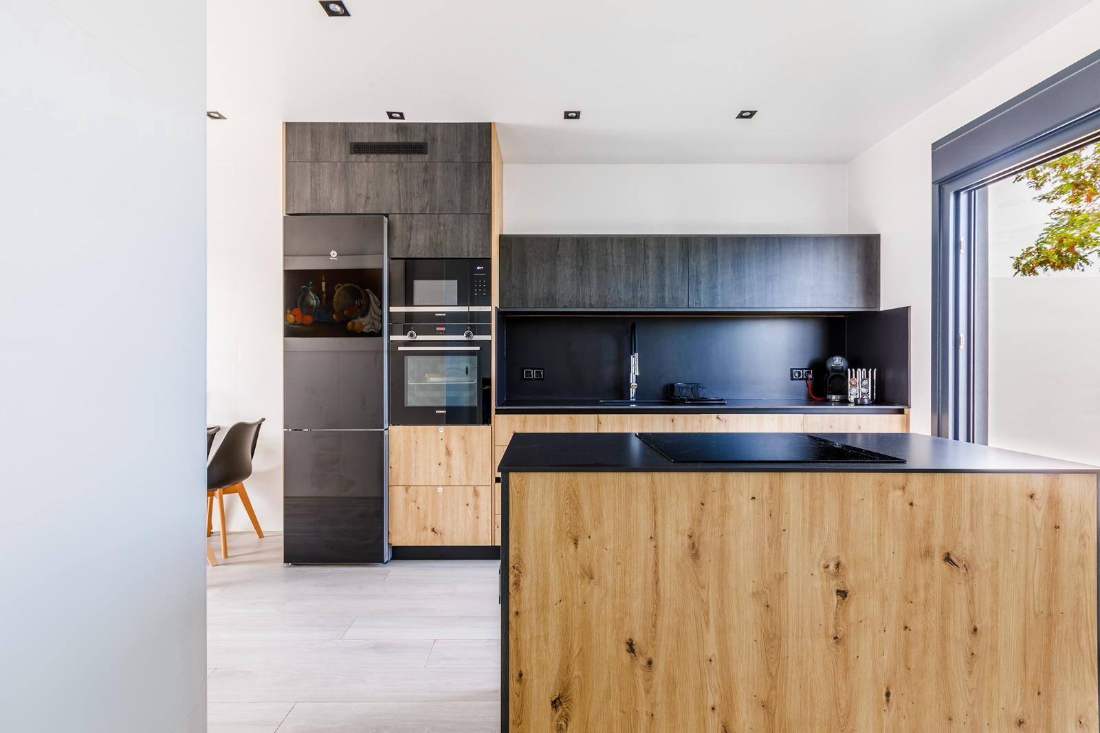 Cocina con isla de madera, encimera negra, horno y frigorífico integrados