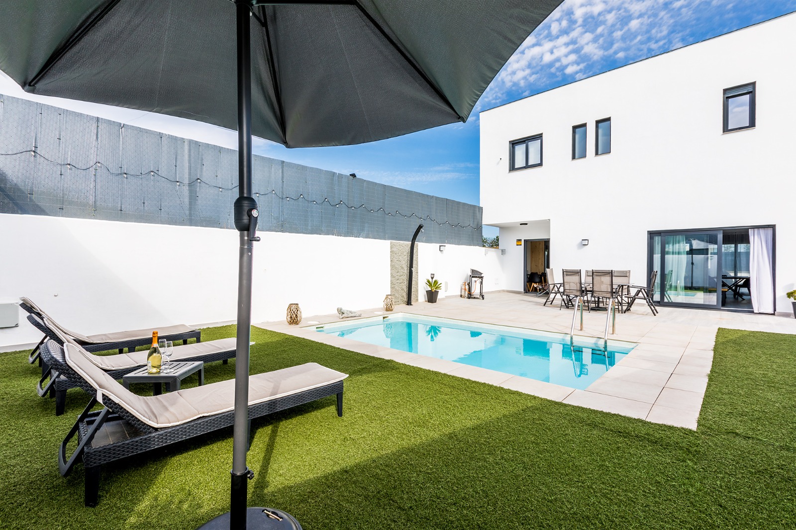 Jardín con césped, sombrilla, tumbonas y piscina junto a la casa