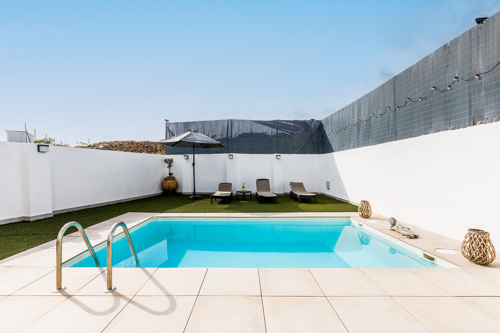 Piscina con escalera de acero y zona de tumbonas