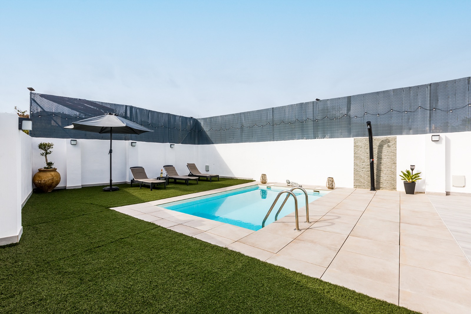 Piscina con jardín, sombrilla y tumbonas