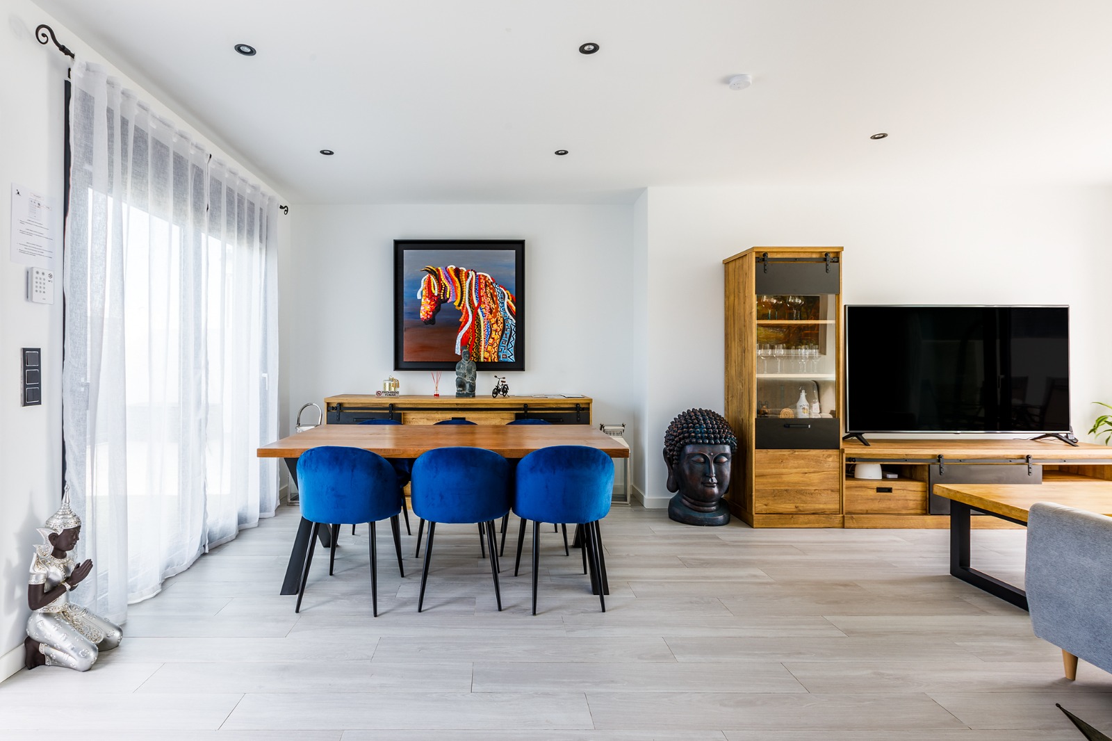 Salón comedor con mesa de madera, sillas azules, televisión y decoración