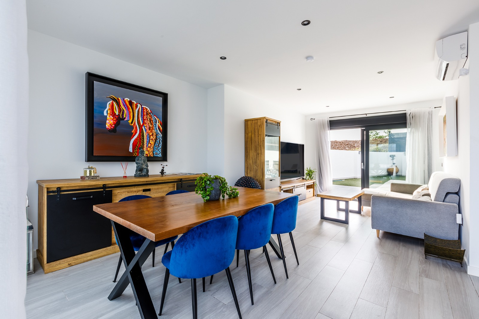 Comedor con mesa de madera y sillas azules junto al salón con salida a la piscina