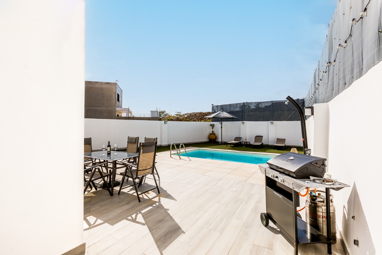 Porche con mesa de comedor y barbacoa junto a la piscina
